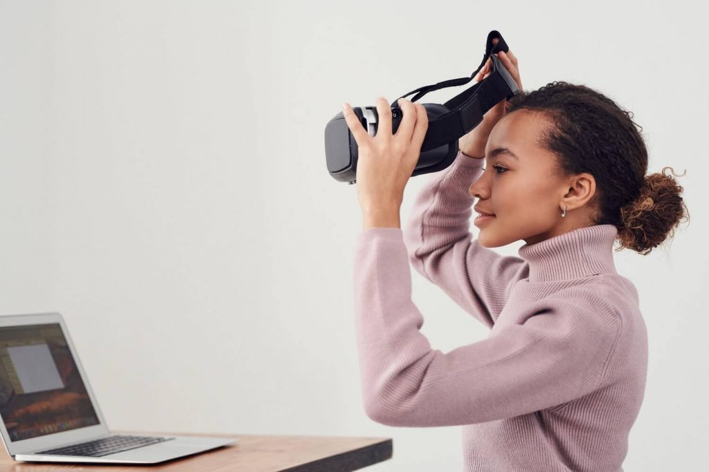 Woman putting on VR headset in front of computer